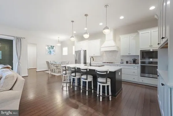 a open kitchen with stainless steel appliances granite countertop a stove a refrigerator a kitchen island a dining table and chairs with wooden floor