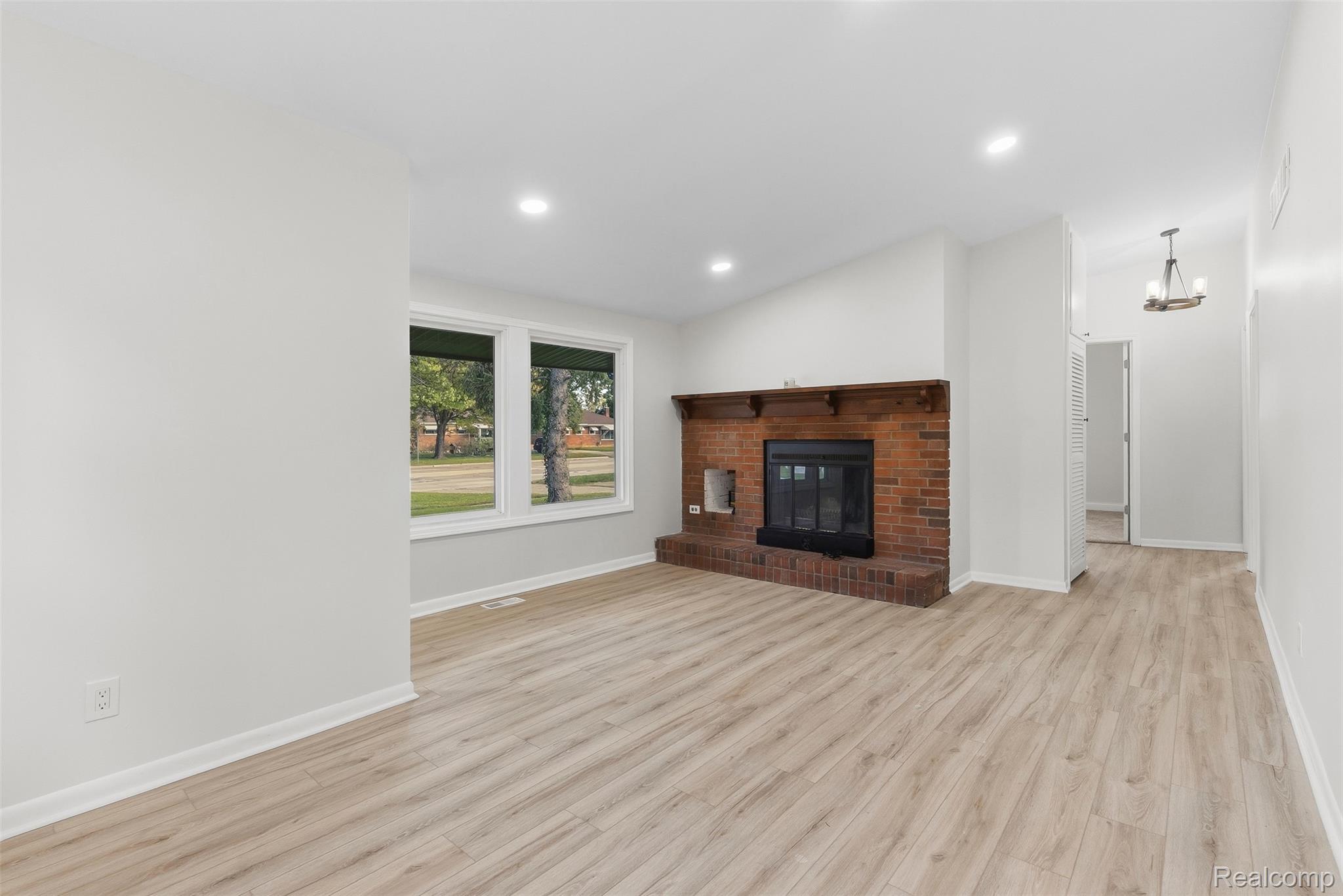 9101 Merriman Road Livonia, MI 48150 - Photo 11 of 41 Recessed lighting, wood-finish flooring, brick fireplace with mantel, window, and a hanging light fixture