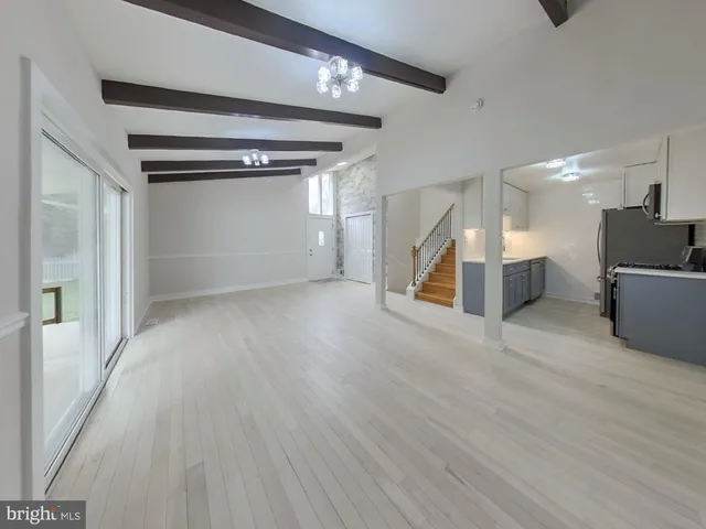 a view of an empty room with wooden floor kitchen view and a window