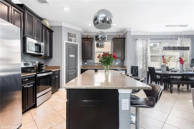 a kitchen with stainless steel appliances kitchen island granite countertop a stove a refrigerator a sink a dining table and chairs with wooden floor