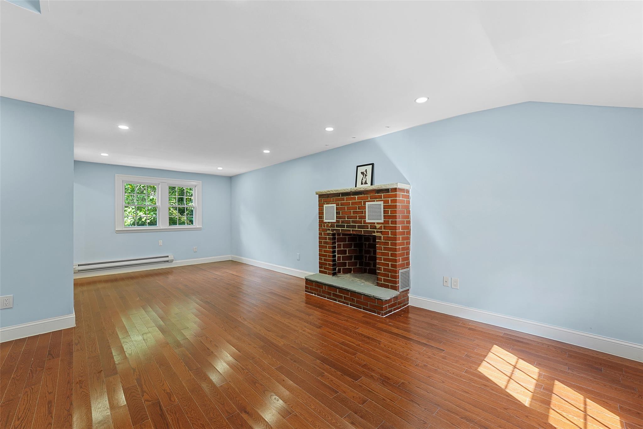 58 Whippoorwill Road East Armonk, NY 10504 - Photo 9 of 22 Unfurnished living room featuring hardwood / wood-style floors, a fireplace, a baseboard heating unit, and recessed lighting
