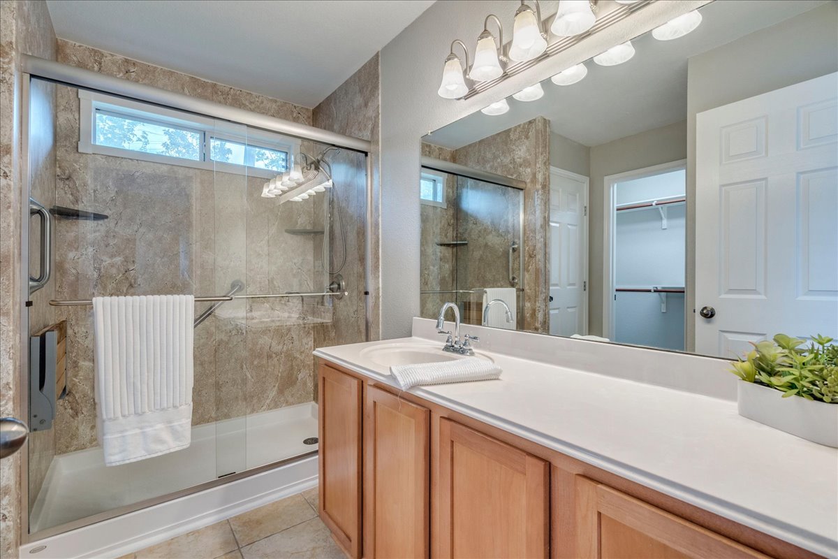 1151 Stone Rim Loop Buda, TX 78610 - Photo 18 of 36 Primary Bathroom featuring a spacious walk-in shower with glass doors and tiled walls, a vanity with a light-colored countertop and wooden cabinetry, and a large mirror with overhead lighting