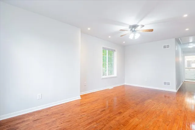 an empty room with wooden floor fan and windows