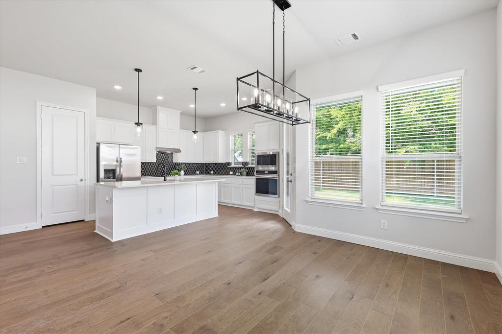 4017 Alpine Street Midlothian, TX 76065 - Photo 11 of 37 Open-concept kitchen and dining area featuring light wood-finish flooring, white cabinetry, a large kitchen island with pendant lighting, built-in stainless steel appliances, and multiple windows with white blinds