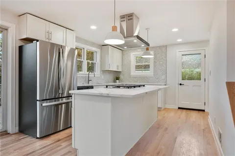 a kitchen with kitchen island granite countertop a refrigerator a sink a center island and wooden floor