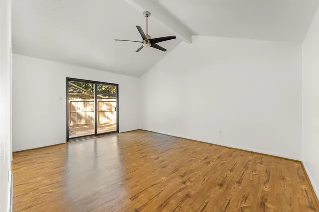 an empty room with wooden floor fan and windows