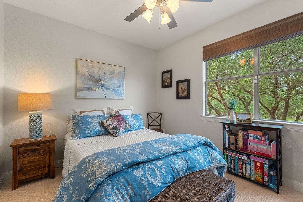 6708 Menchaca Road, Unit 2 Austin, TX 78745 - Photo 18 of 30 Bright bedroom featuring a large window with natural light, a ceiling fan with integrated lighting, a built-in wood-finish shelving unit, and textured wall-to-wall carpeting