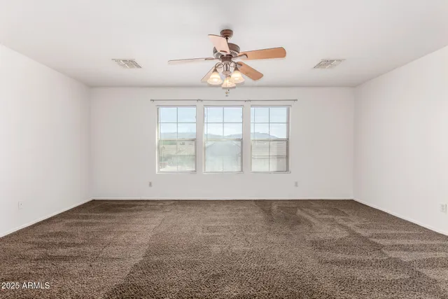 an empty room with chandelier fan and windows