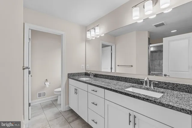 a bathroom with a granite countertop double vanity sink a mirror and a toilet
