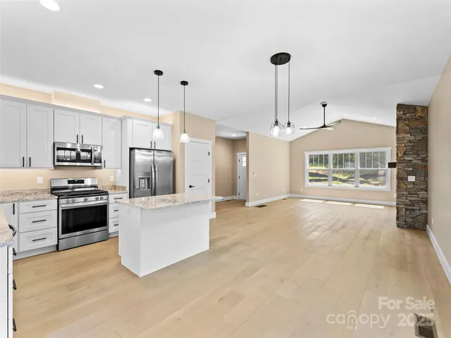 a large kitchen with kitchen island a stove a sink dishwasher a refrigerator and a fireplace with wooden floor