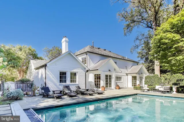 a view of a white house with a large pool lawn chairs and a fire pit