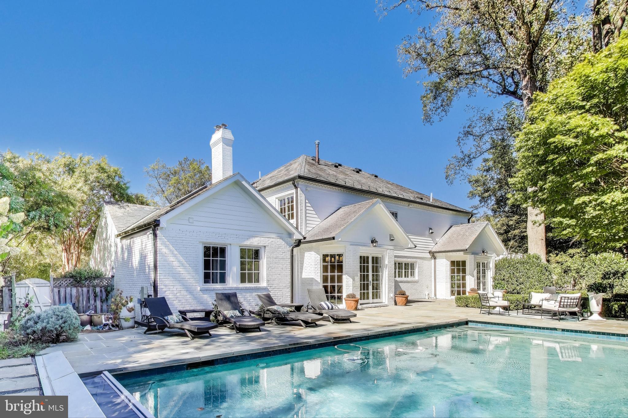 a view of a white house with a large pool lawn chairs and a fire pit
