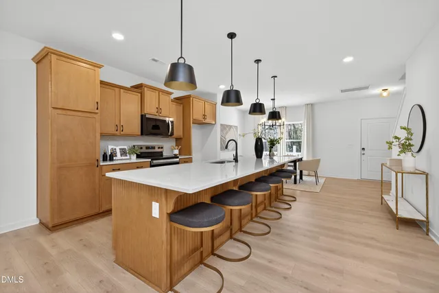 a kitchen with stainless steel appliances a stove a refrigerator a sink a dining table and chairs with wooden floor