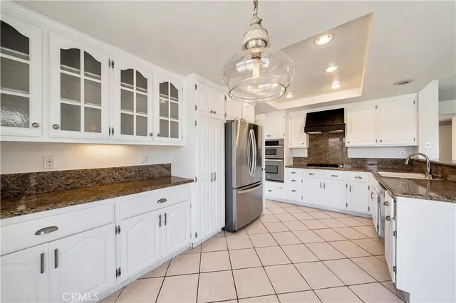 a kitchen with stainless steel appliances granite countertop a refrigerator a sink dishwasher a stove and white cabinets with wooden floor