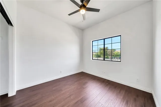 an empty room with wooden floor chandelier fan and windows