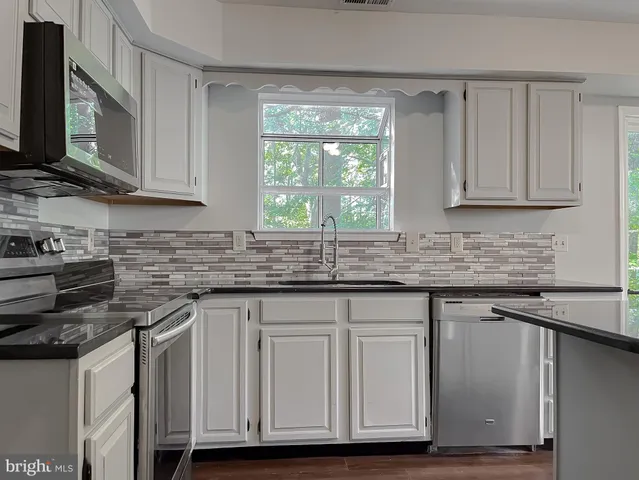 a kitchen with granite countertop wooden floors a stove and a microwave