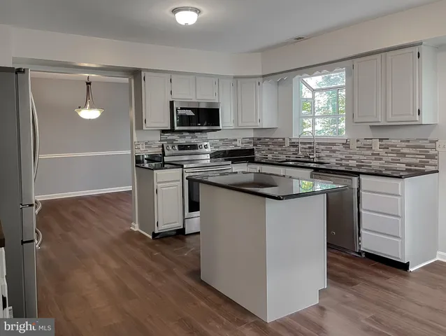 a kitchen with stainless steel appliances granite countertop a stove a sink dishwasher a refrigerator and white cabinets with wooden floor