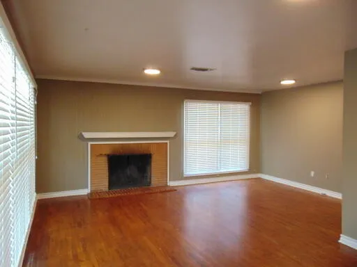 an empty room with wooden floor fireplace and windows