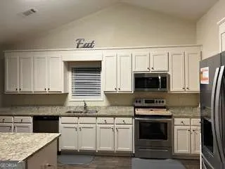 a kitchen with granite countertop a sink stainless steel appliances and white cabinets