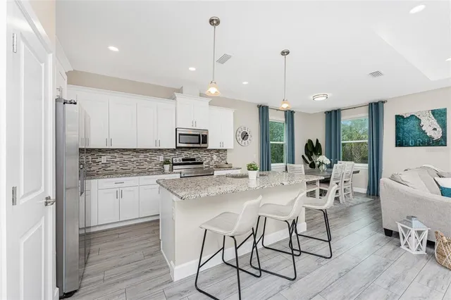 a kitchen with stainless steel appliances kitchen island granite countertop a dining table chairs stove and white cabinets