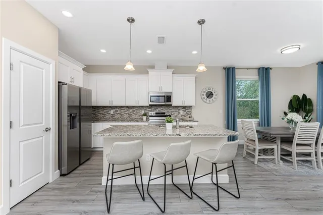 a kitchen with stainless steel appliances kitchen island granite countertop a dining table chairs and white cabinets