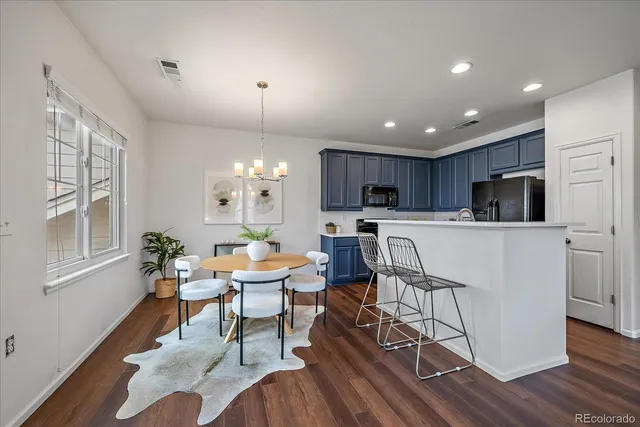 a kitchen with stainless steel appliances kitchen island granite countertop a stove a refrigerator a sink a dining table and chairs with wooden floor