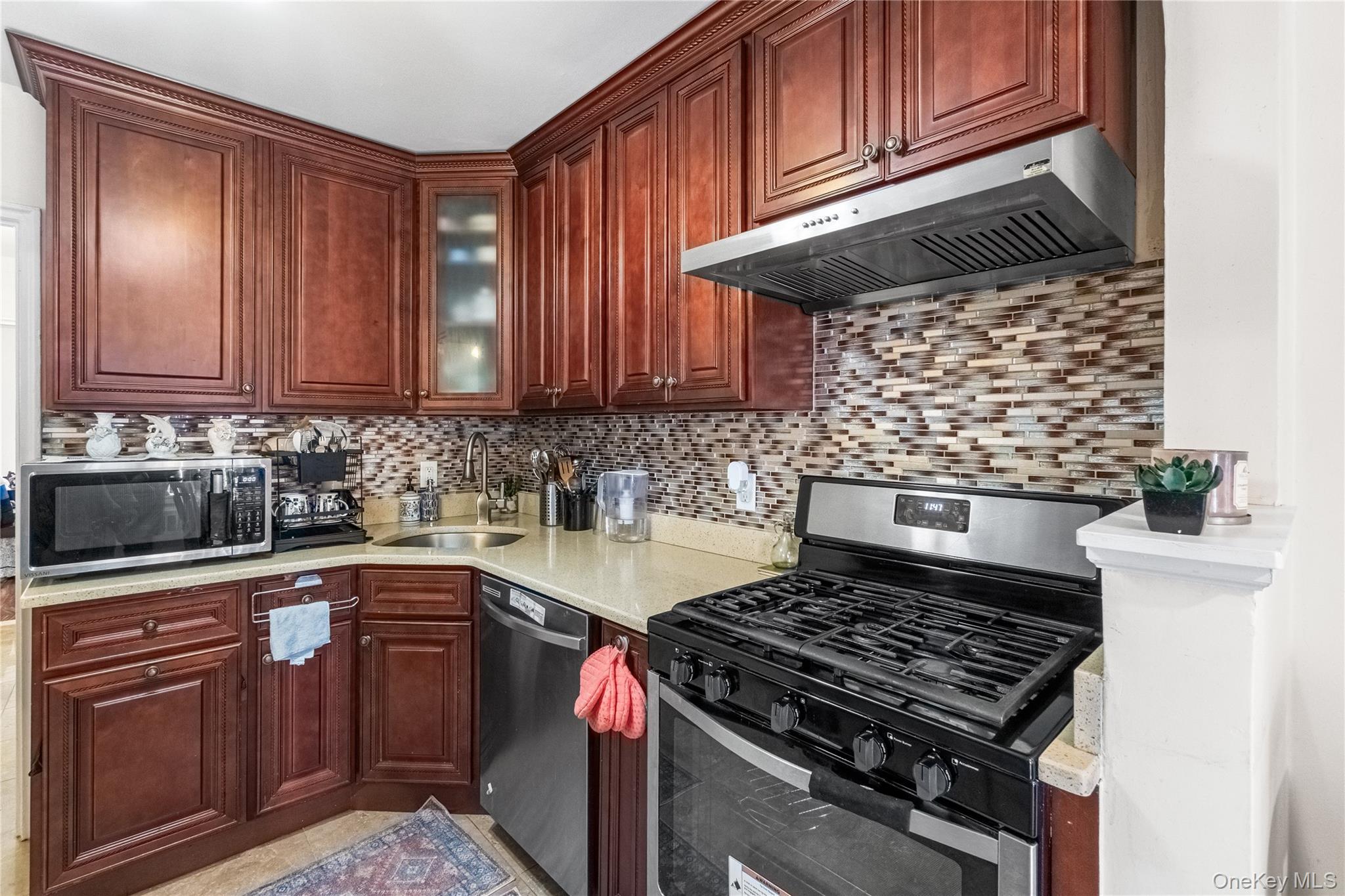 203-10 Murdock Avenue Queens, NY 11412 - Photo 11 of 18 Kitchen with stainless steel appliances, under cabinet range hood, glass insert cabinets, light stone countertops, and backsplash