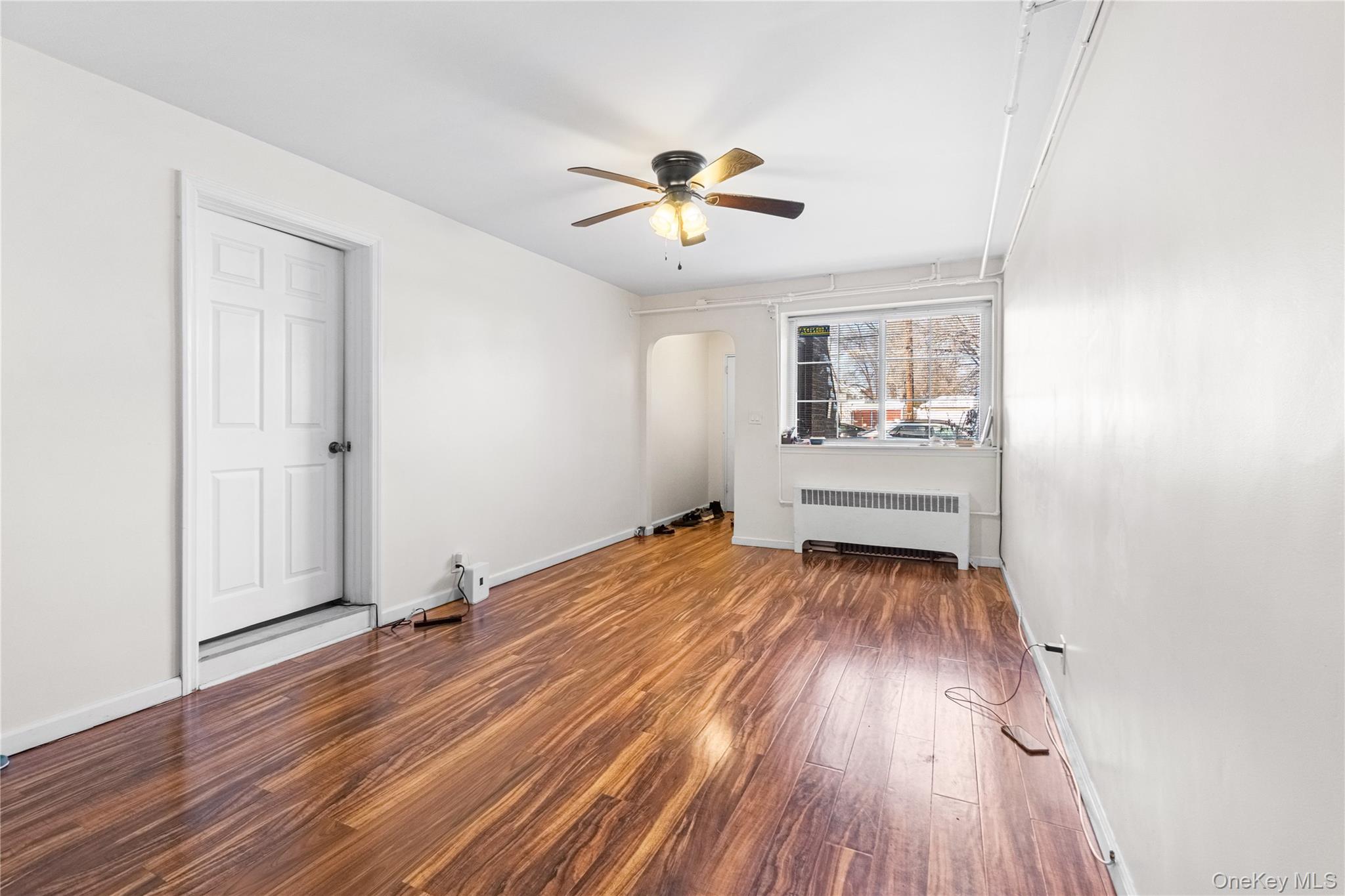 203-10 Murdock Avenue Queens, NY 11412 - Photo 3 of 18 Unfurnished room featuring arched walkways, radiator heating unit, hardwood / wood-style flooring, and a ceiling fan