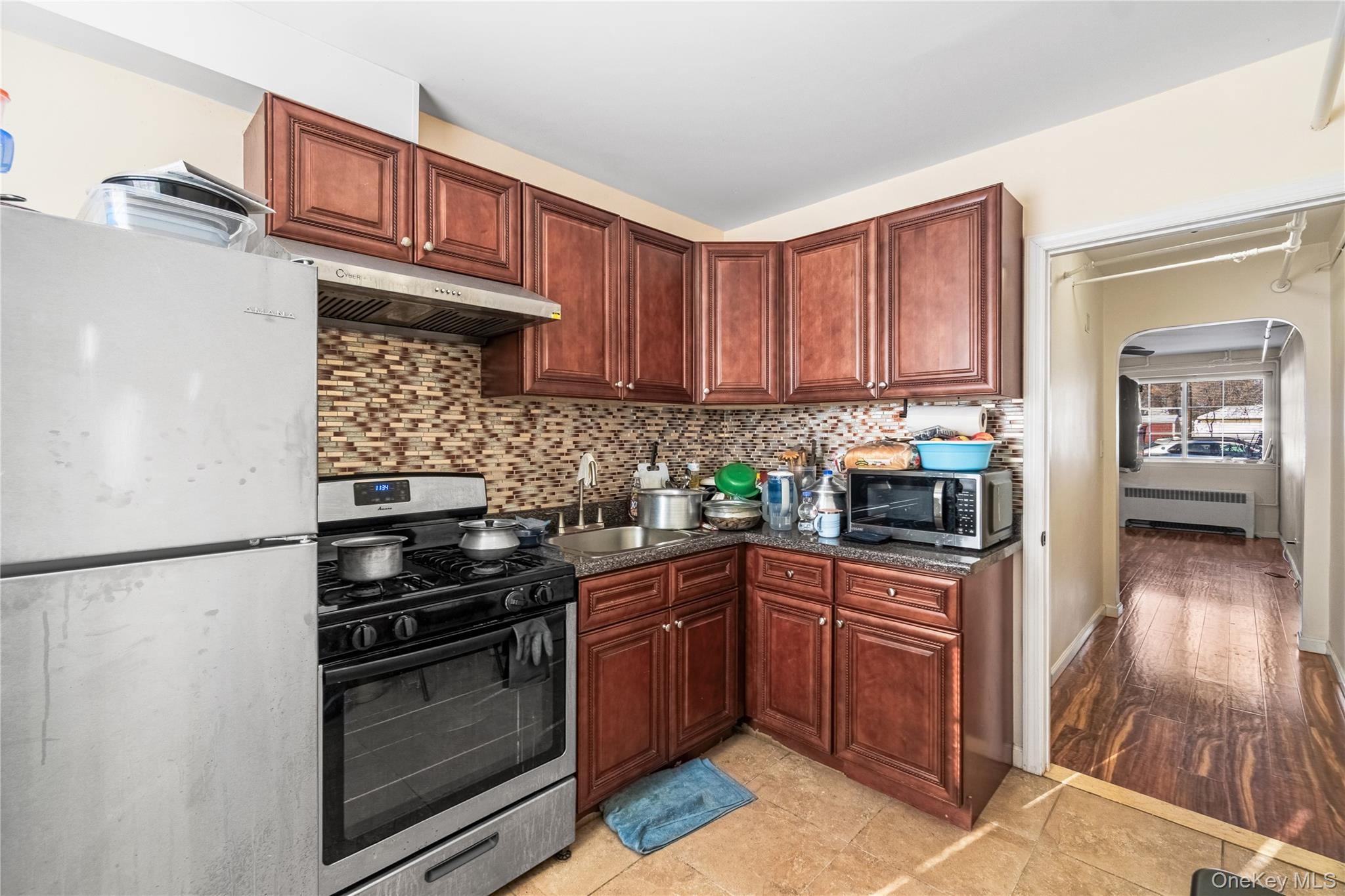 203-10 Murdock Avenue Queens, NY 11412 - Photo 6 of 18 Kitchen with stainless steel appliances, arched walkways, backsplash, radiator heating unit, and under cabinet range hood