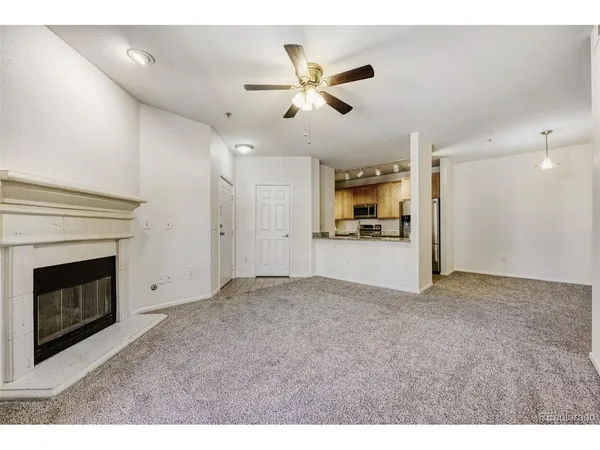 a view of a livingroom with a fireplace a ceiling fan and kitchen view
