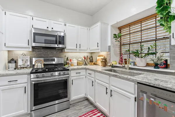 a kitchen with stainless steel appliances granite countertop white cabinets a stove a sink and a microwave