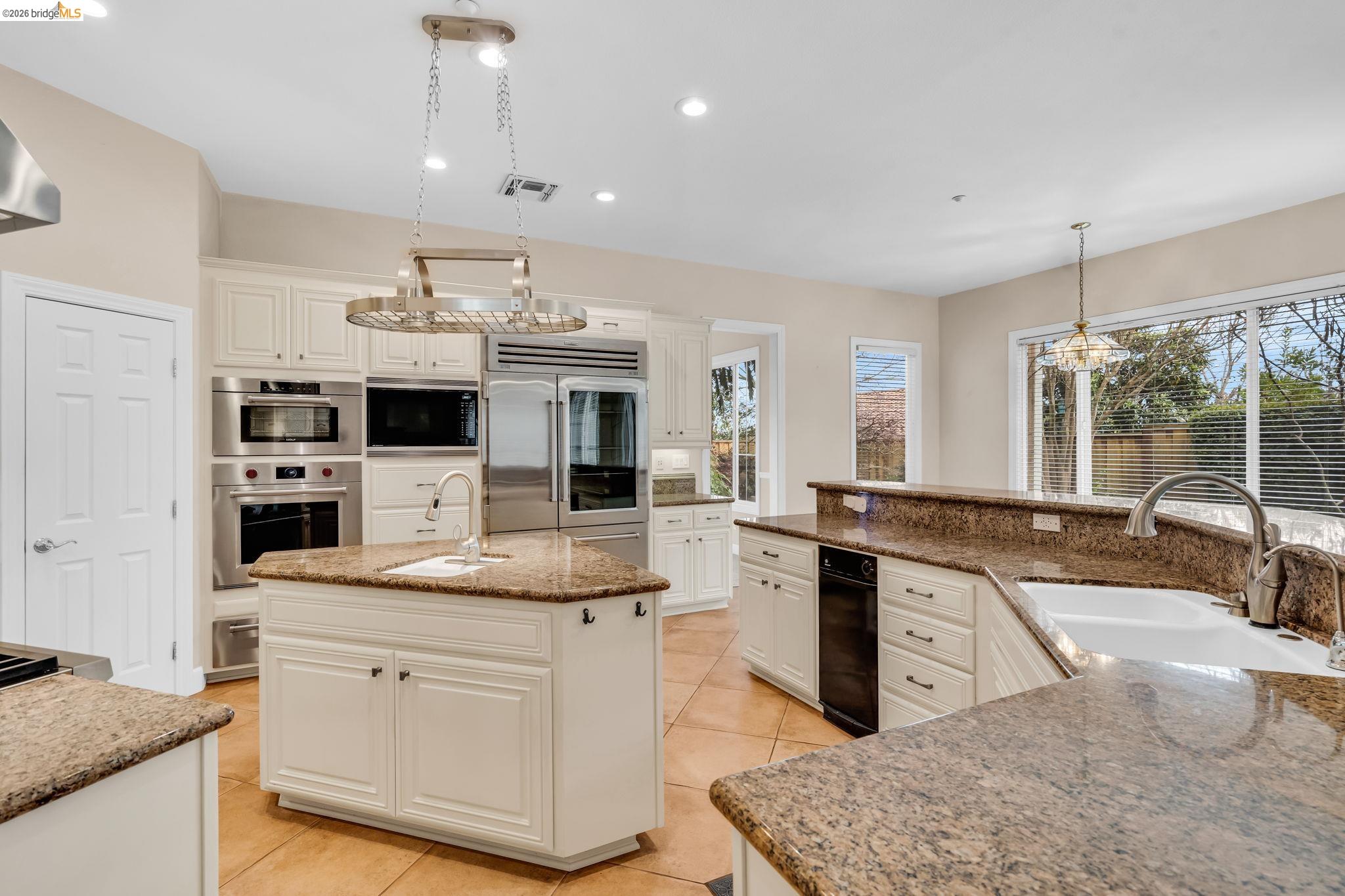 5 Circle E Ranch Place San Ramon, CA 94583 - Photo 49 of 60 Kitchen featuring an island with sink, light stone counters, suspended lighting, built in appliances, and white cabinetry