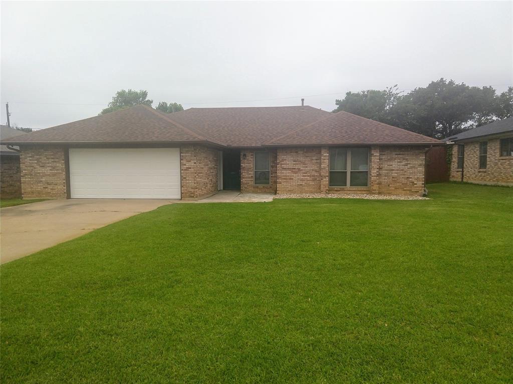 Ranch-style home featuring an attached garage, driveway, a front yard, roof with shingles, and brick siding