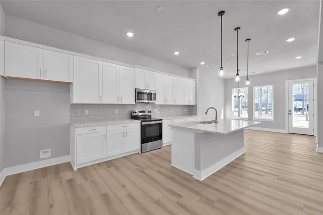 a large white kitchen with kitchen island a sink dishwasher a stove and white cabinets with wooden floor
