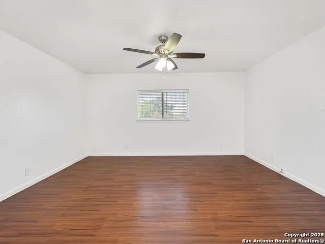 an empty room with wooden floor fan and windows