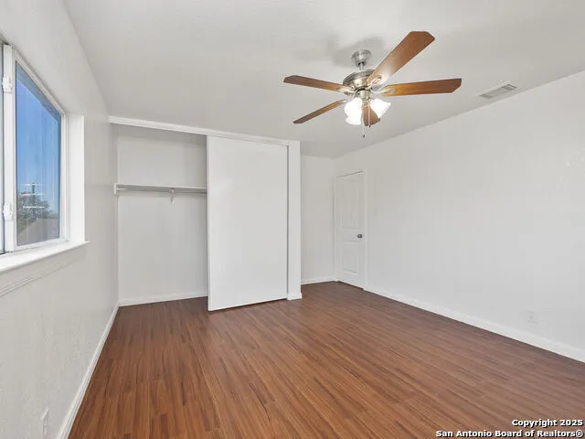 a view of an empty room with wooden floor and a ceiling fan