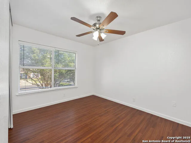 an empty room with wooden floor fan and windows
