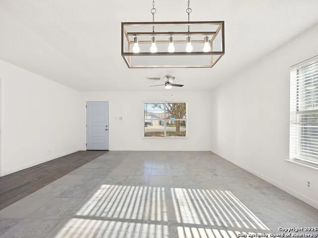 an empty room with a chandelier fan and windows