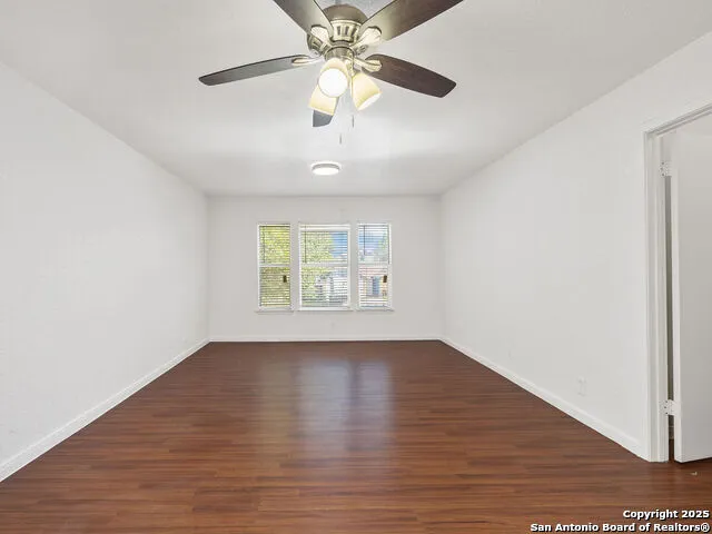 an empty room with wooden floor chandelier fan and windows