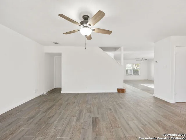 an empty room with wooden floor a ceiling fan and windows