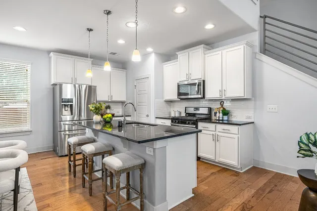 a kitchen with stainless steel appliances kitchen island granite countertop a stove a sink a refrigerator white cabinets and wooden floor