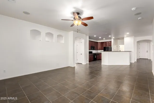 a view of an empty room with wooden floor and a kitchen view