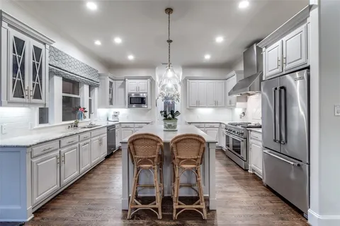 a kitchen with stainless steel appliances granite countertop a kitchen island a stove a refrigerator a oven a sink with island chairs and wooden cabinets
