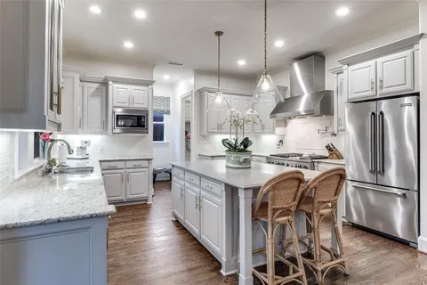 a kitchen with stainless steel appliances granite countertop a sink a stove a refrigerator cabinets and chairs