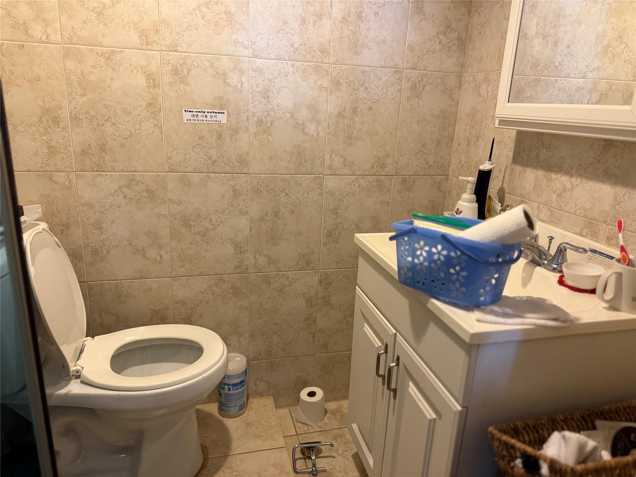 81-09 41st Avenue, Unit 5B Queens, NY 11373 - Photo 7 of 25 Half bath with tile walls, vanity, tile patterned floors, and toilet