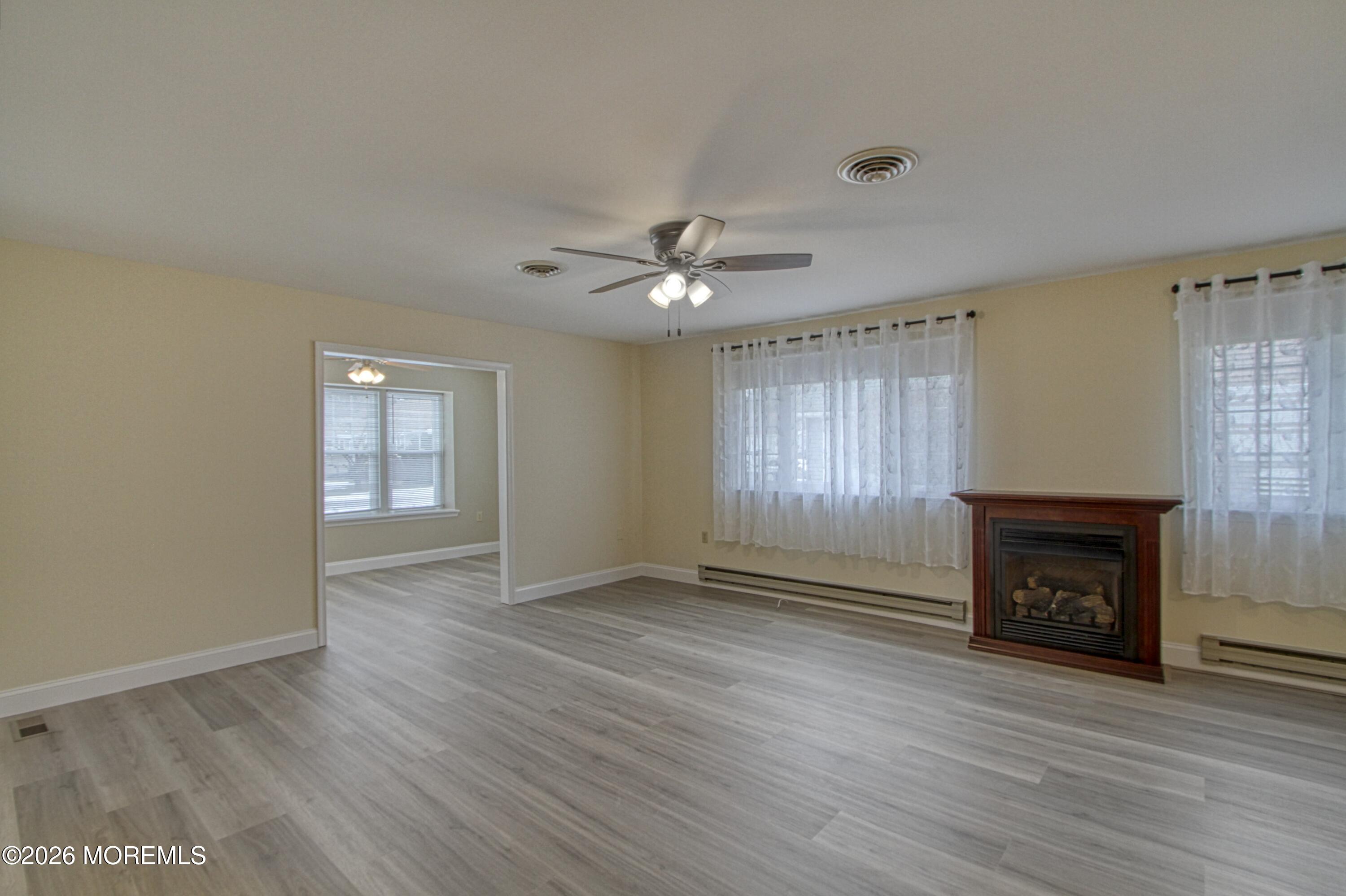 111 Sunset Road, Unit 60 Whiting, NJ 08759 - Photo 21 of 23 an empty room with windows a fireplace a ceiling fan and wooden floor