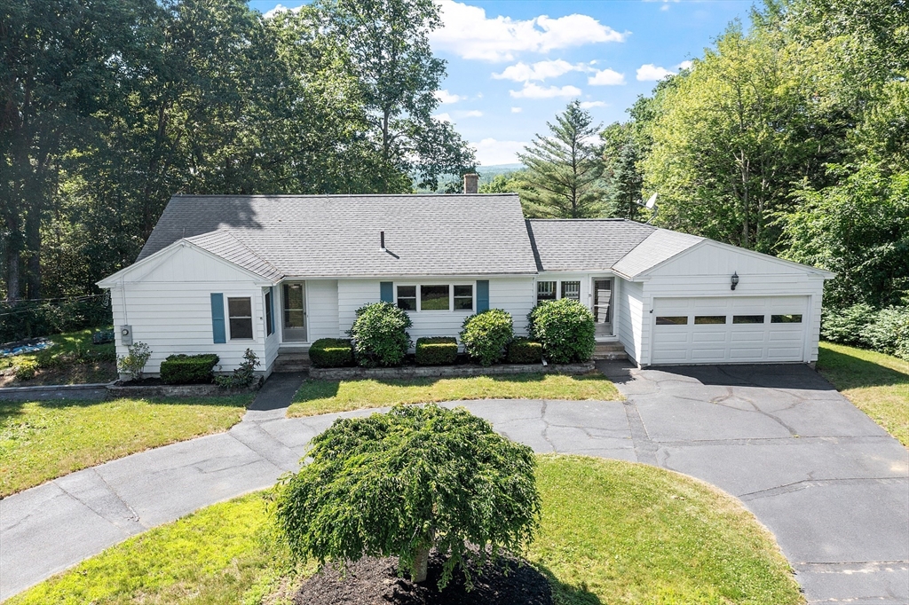 a view of a white house with a yard plants and large tree