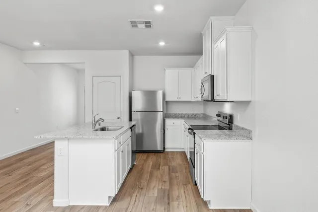 a kitchen with a sink a refrigerator a stove and white cabinets with wooden floor