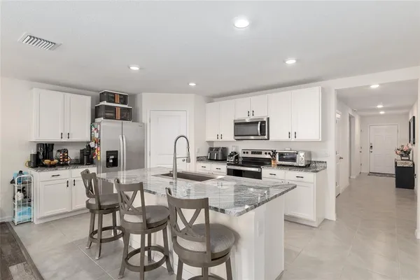 a large kitchen with stainless steel appliances granite countertop a stove a sink a refrigerator and a granite counter tops with white cabinets