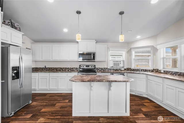 a kitchen with stainless steel appliances granite countertop a stove a sink a refrigerator and white cabinets with wooden floor